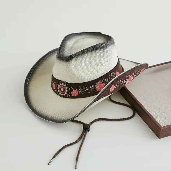 White cowboy sun hat with dark brown floral band and decorative tie strings