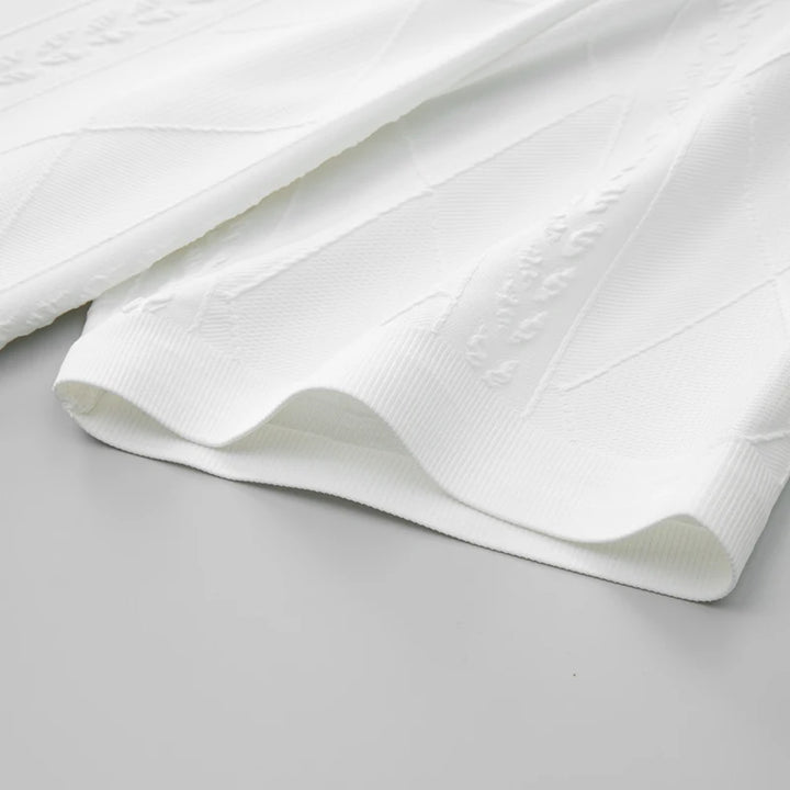 White knit shirt fabric with raised diamond-and-stitched texture along the hem
