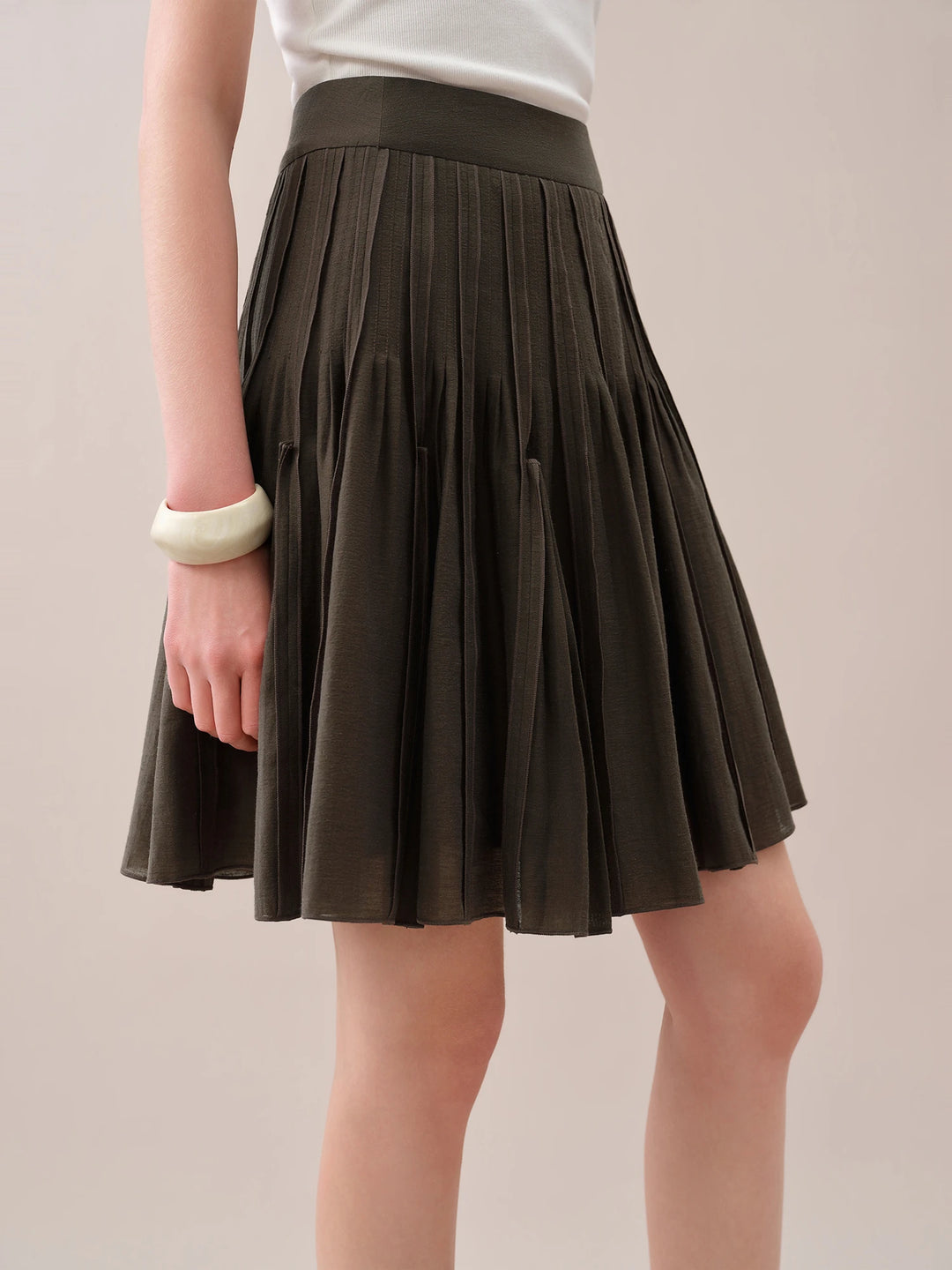 Side view of dark brown pleated mini skirt with flared hem and elastic waistband