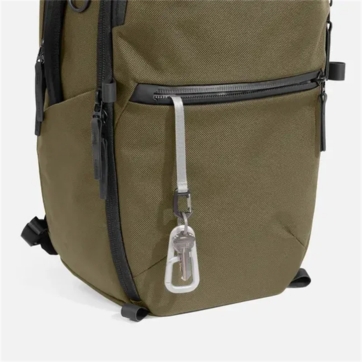 Olive green nylon backpack with front zip pocket, adjustable straps, and key clip
