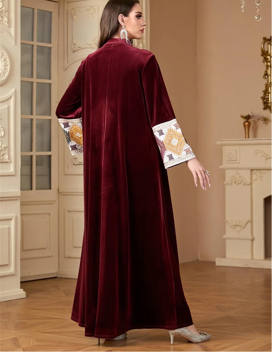Woman wearing a burgundy abaya with embroidered sleeves in an elegant interior setting.
