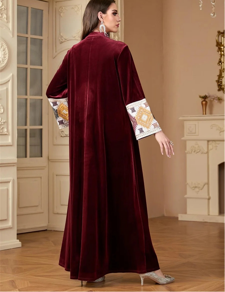 Woman wearing a burgundy abaya with embroidered sleeves in an elegant interior setting.