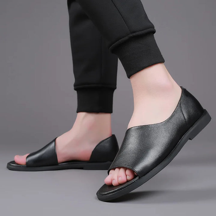 Black leather slide sandals with open toe, worn with black joggers