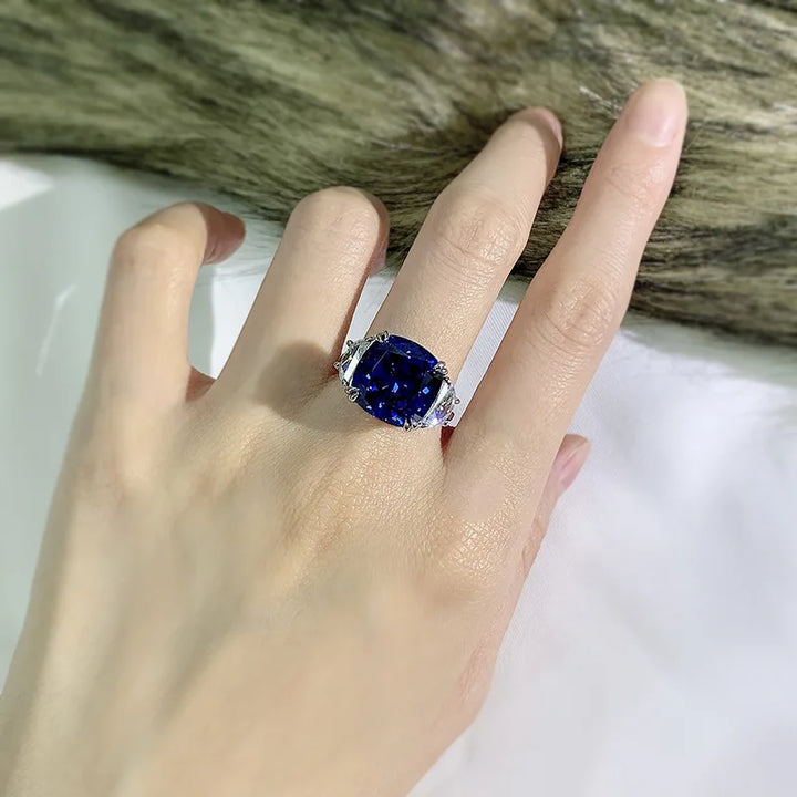 Sterling silver ring on hand with blue oval center stone and clear side accents