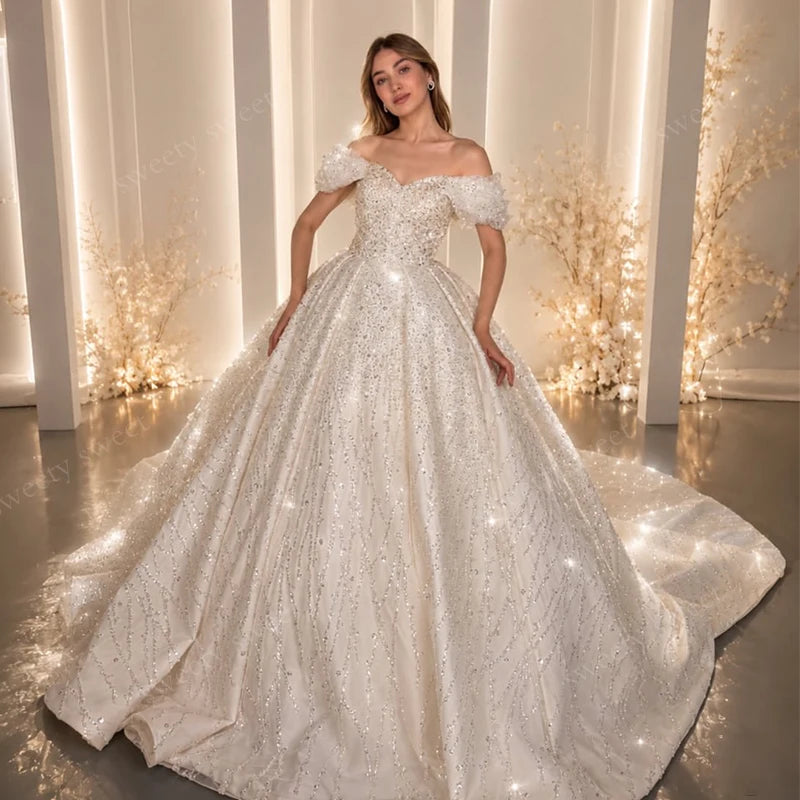 Beaded lace wedding gown with off-shoulder neckline, sheer sleeves, full sparkling skirt