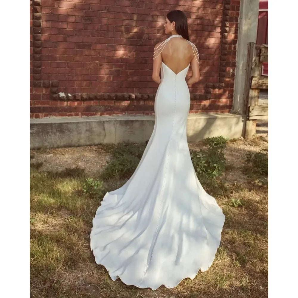 White wedding dress with open back and long train on a person standing outdoors.