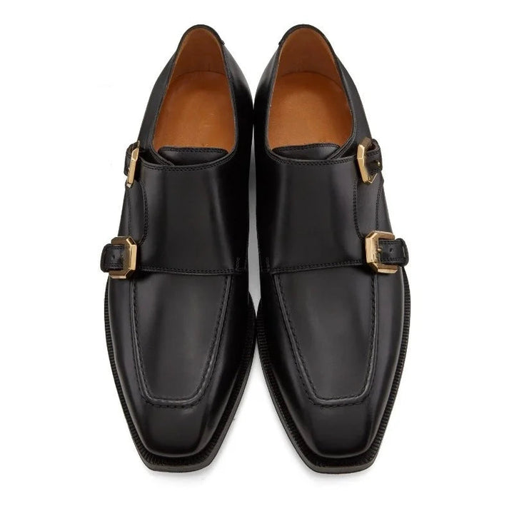 Pair of black leather shoes with gold buckles on a white background, branded 'Stiglitz'.