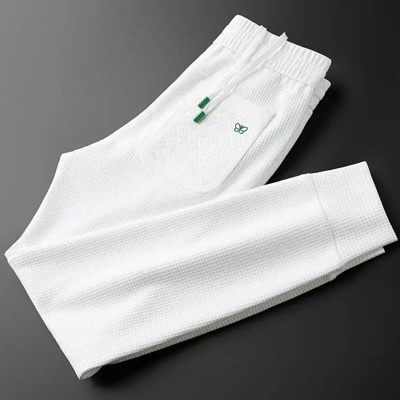 White cotton track pants, folded view showing waistband area and small green logo