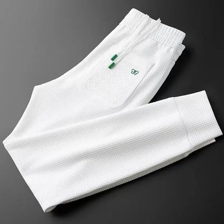 White cotton track pants, folded view showing waistband area and small green logo