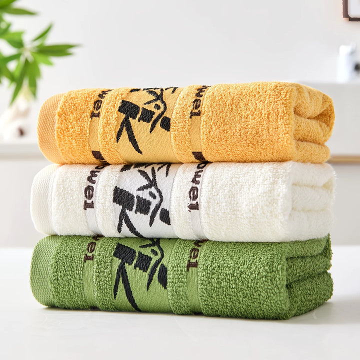 3-piece cotton bathroom towel set stacked in golden yellow, white, and green with bamboo print