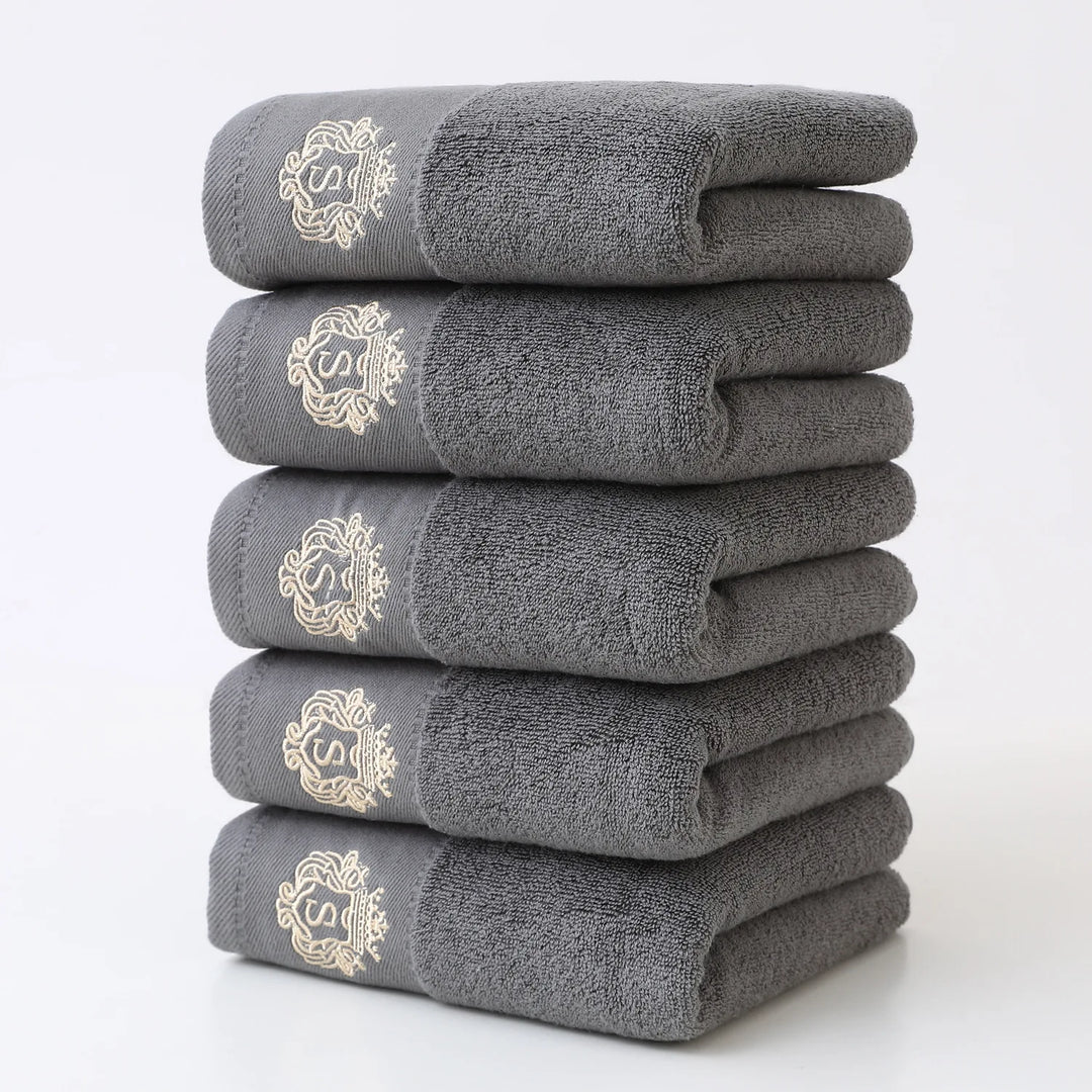 Gray 5-piece bathroom towel set with gold monogram, neatly folded stack of towels