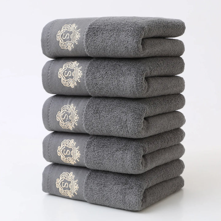 Gray 5-piece bathroom towel set with gold monogram, neatly folded stack of towels
