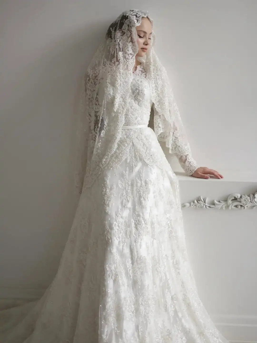 Ivory lace A-line wedding dress with sheer long sleeves, high neckline, and fitted waist.