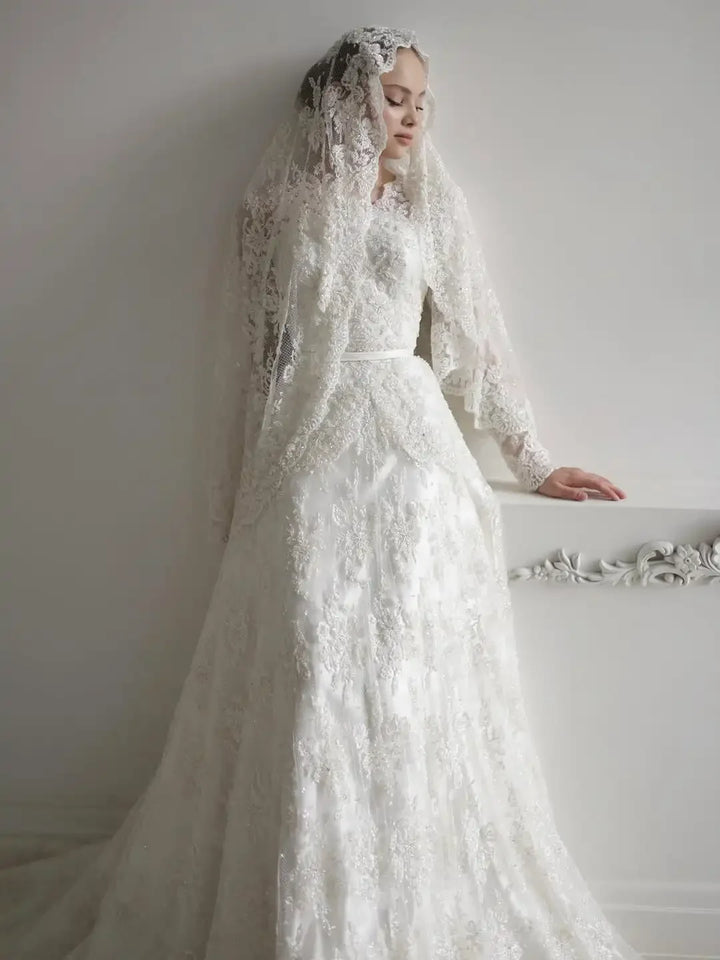 Ivory lace A-line wedding dress with sheer long sleeves, high neckline, and fitted waist.