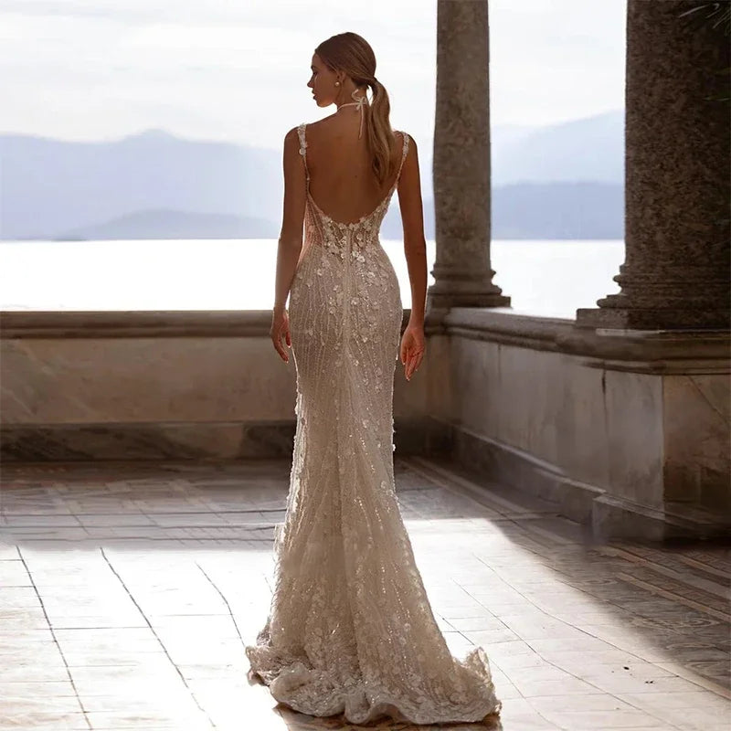 Woman in a white lace wedding dress standing on a sunlit terrace with columns and mountains in the background.