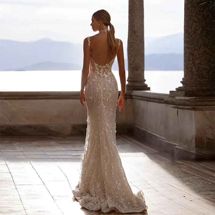 Woman in a white lace wedding dress standing on a sunlit terrace with columns and mountains in the background.