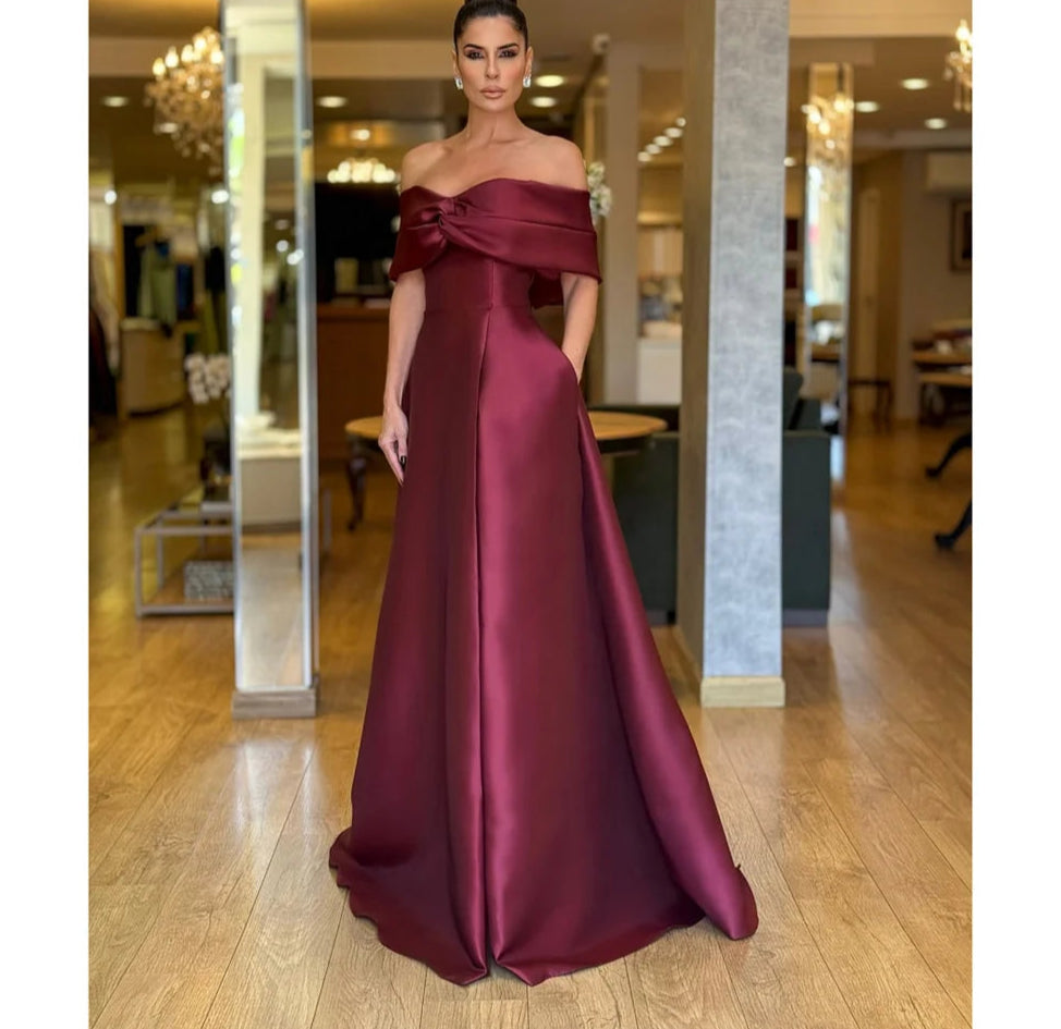 Woman in a burgundy off-shoulder gown standing in an indoor setting.