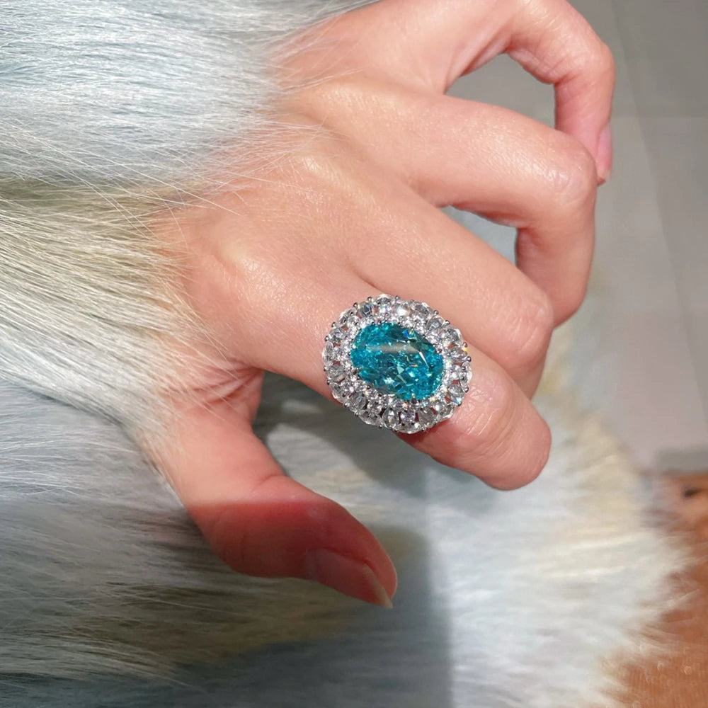 Sterling silver blue-teal oval gemstone ring with crystal halo, close-up on hand
