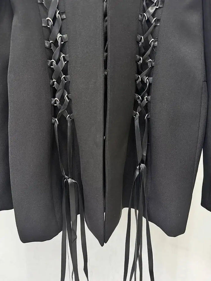 Close-up of black blazer front with vertical lace-up panels and hanging fringe cords