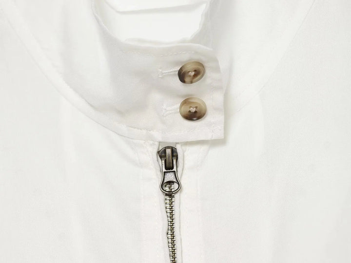 Close-up of white stand-collar jacket: brown buttons and metal zipper with pull tab