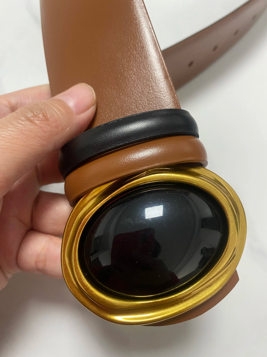 Wide leather belt, tan-brown, with oval black center buckle wrapped in gold-tone frame