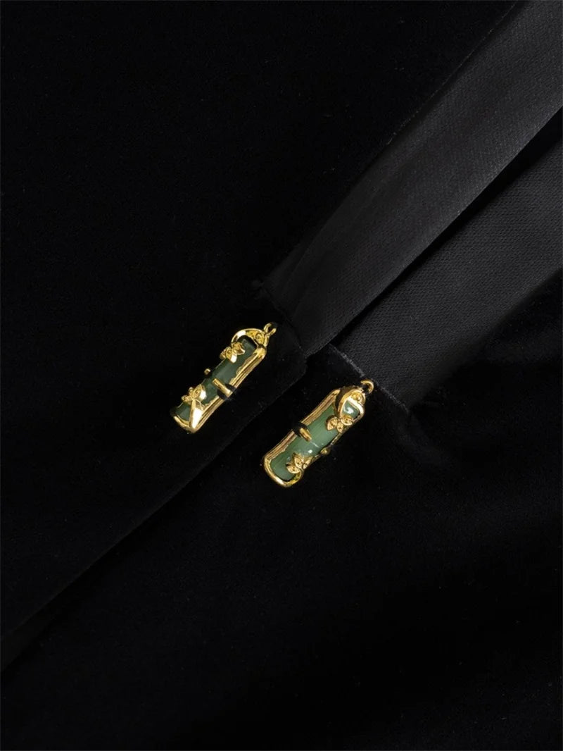 Close-up of black vest jacket front clasp details, gold hardware with green accents