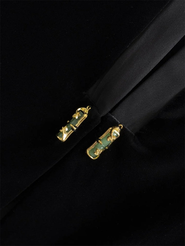 Close-up of black vest jacket front clasp details, gold hardware with green accents
