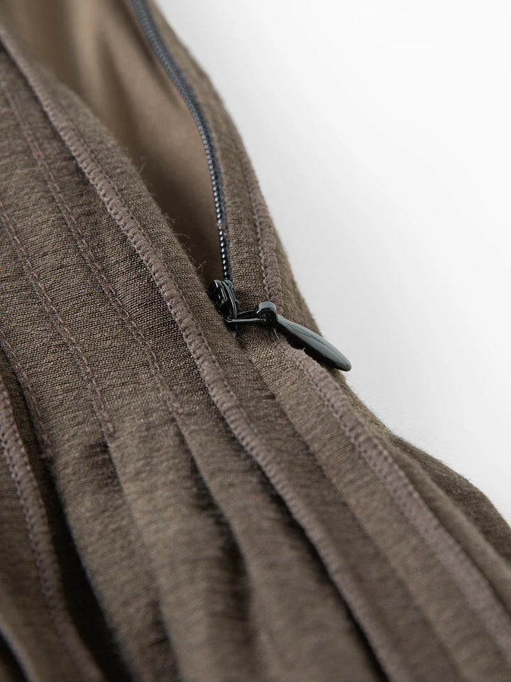 Close-up of dark brown pleated skirt seam with black adjustable clasp detail