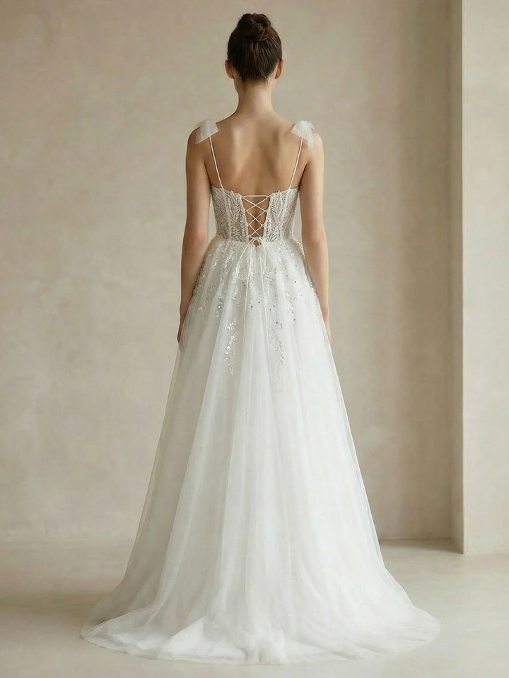 White beaded bridal gown with open-back corset and spaghetti straps, flowing tulle skirt