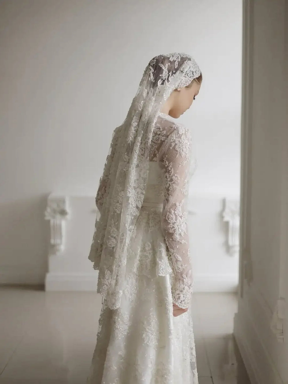 Ivory lace A-line wedding dress with long lace sleeves and tiered full skirt, side view.