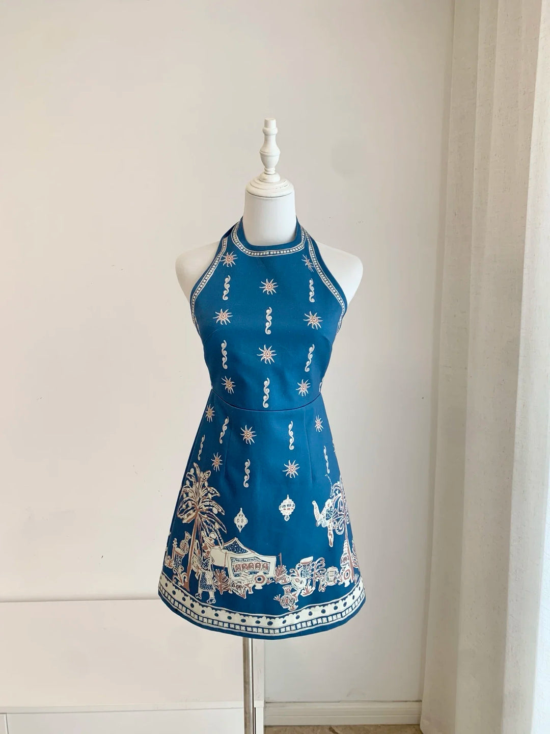 Blue halter neck mini dress front view with gold-and-white scroll and motif print