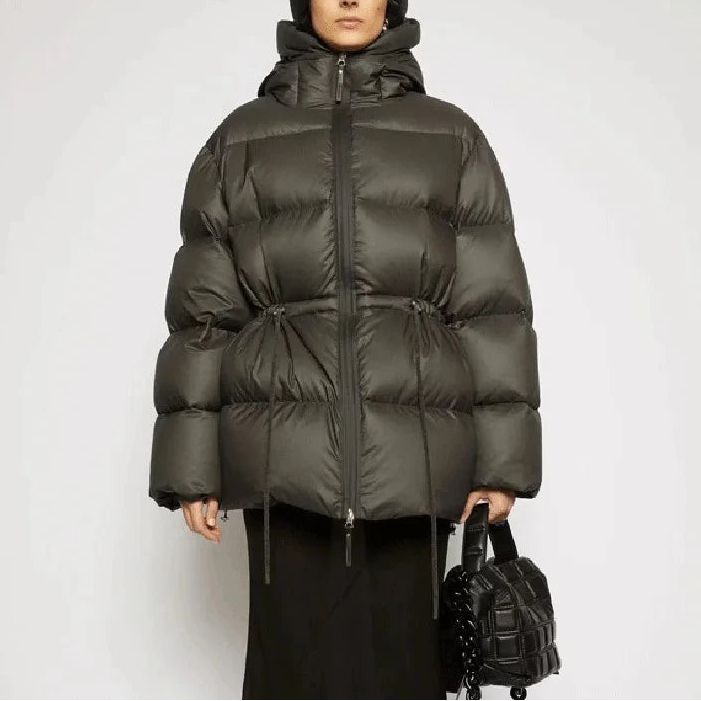 Person wearing a green puffer jacket holding a black bag on a white background