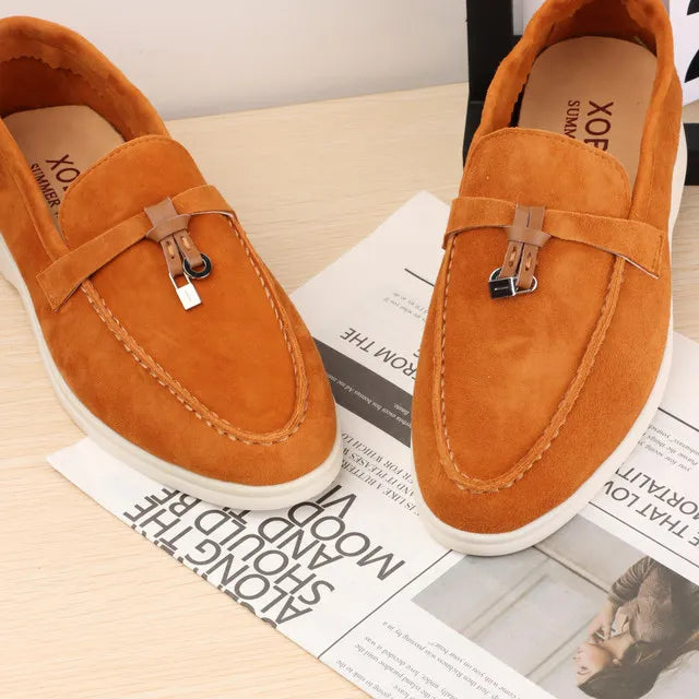 Orange suede slip-on loafers with metal buckle strap and white rubber sole.