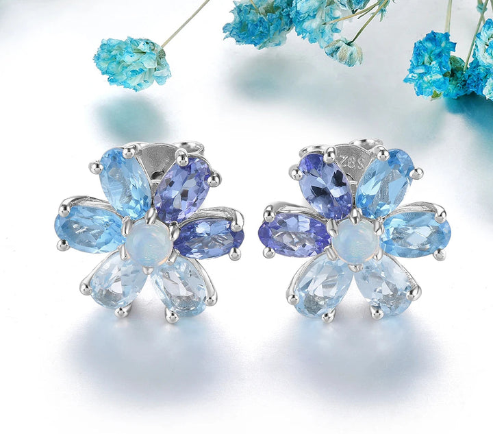 Pair of earrings with blue gemstones on a white background with blue flowers.