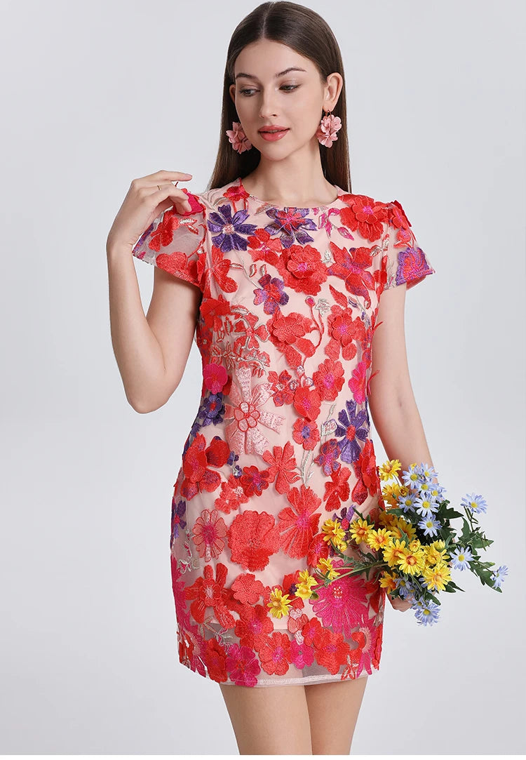 Woman wearing a colorful floral dress holding flowers against a plain background