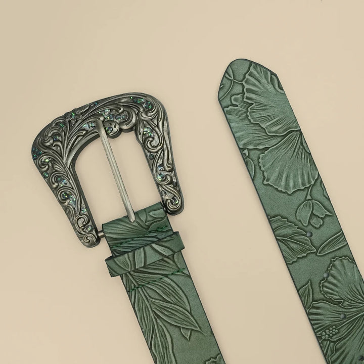 Ornate silver belt buckle with green leaf-embossed strap close-up