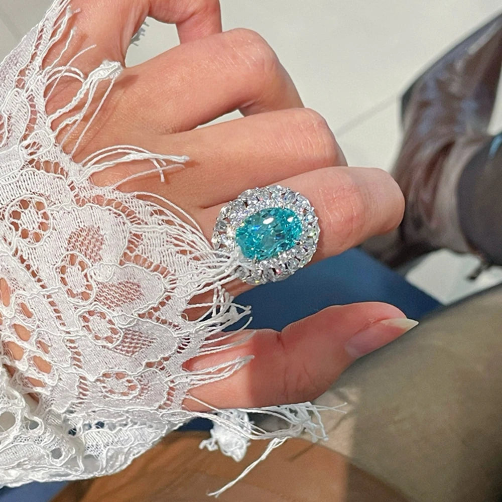 Sterling silver blue-teal oval gemstone ring with round crystal halo, on finger