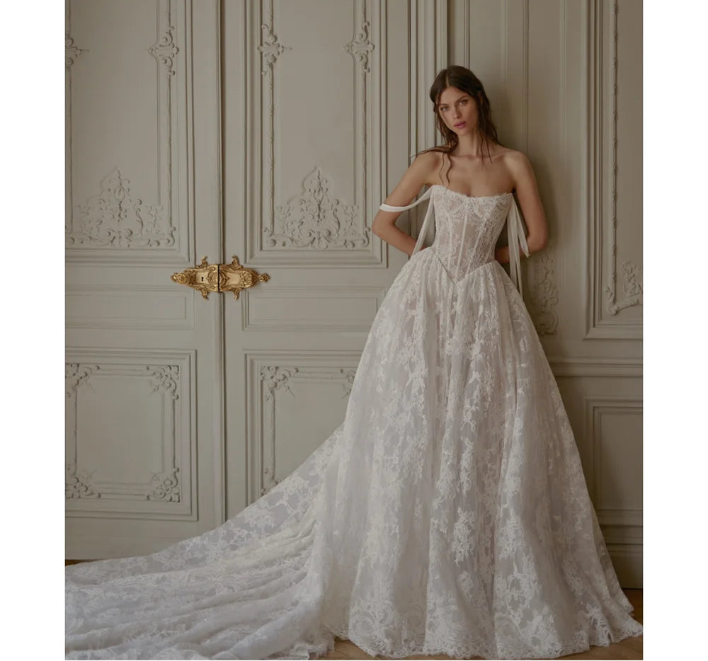 Woman in a white lace wedding dress standing against an ornate wall.
