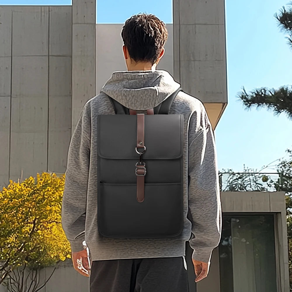 Black minimalist backpack with front flap and brown strap, worn from behind