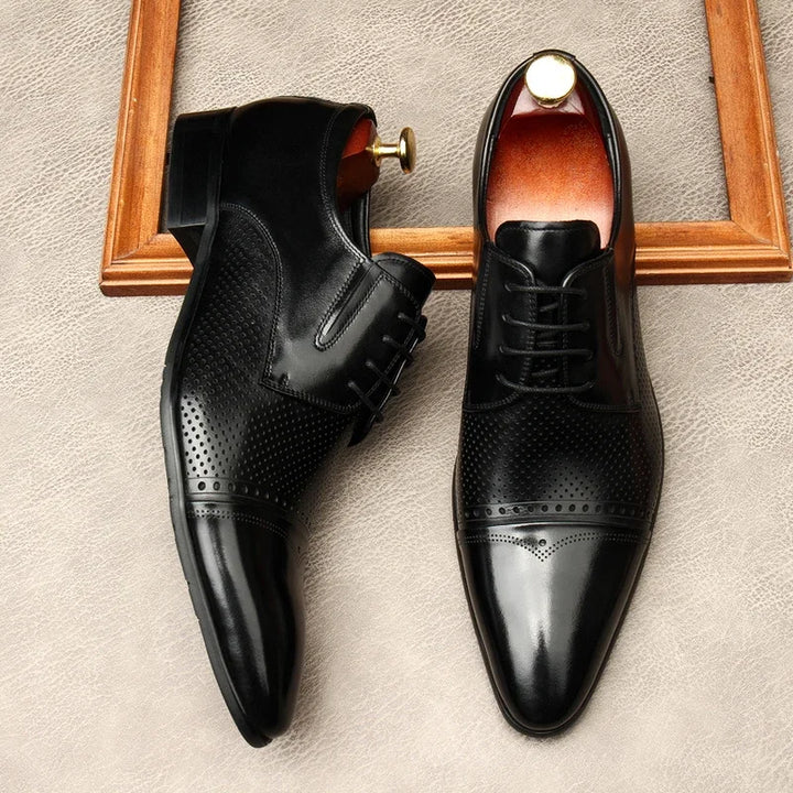 Pair of black lace-up dress shoes on a textured surface, side views