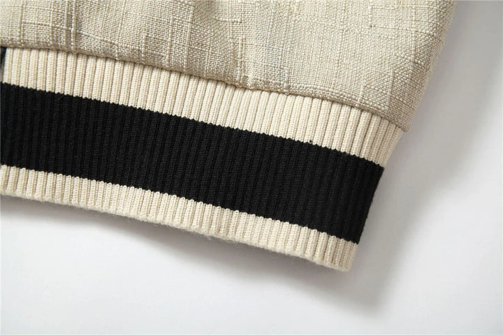 Ribbed hem of black and cream varsity baseball coat with knit striped band