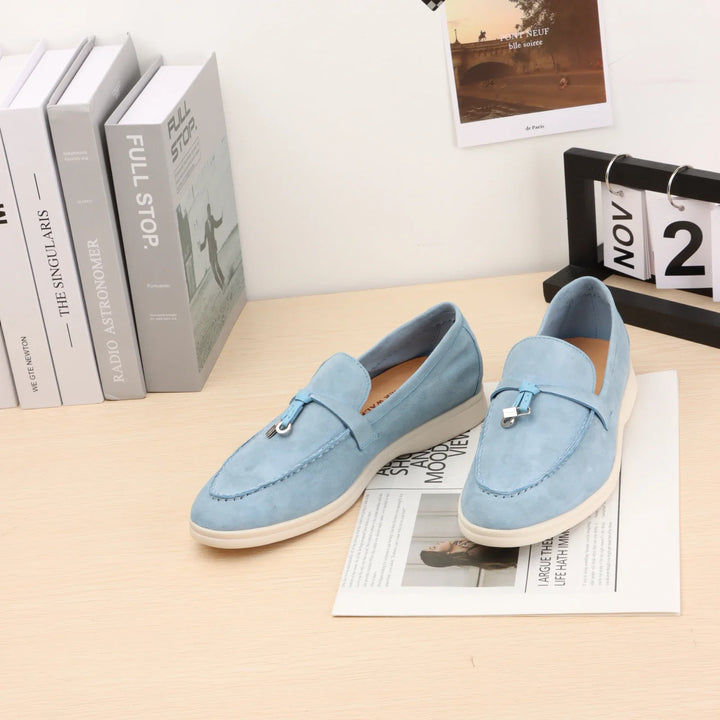 Light blue suede slip-on loafers with metal bit detail and white rubber sole.