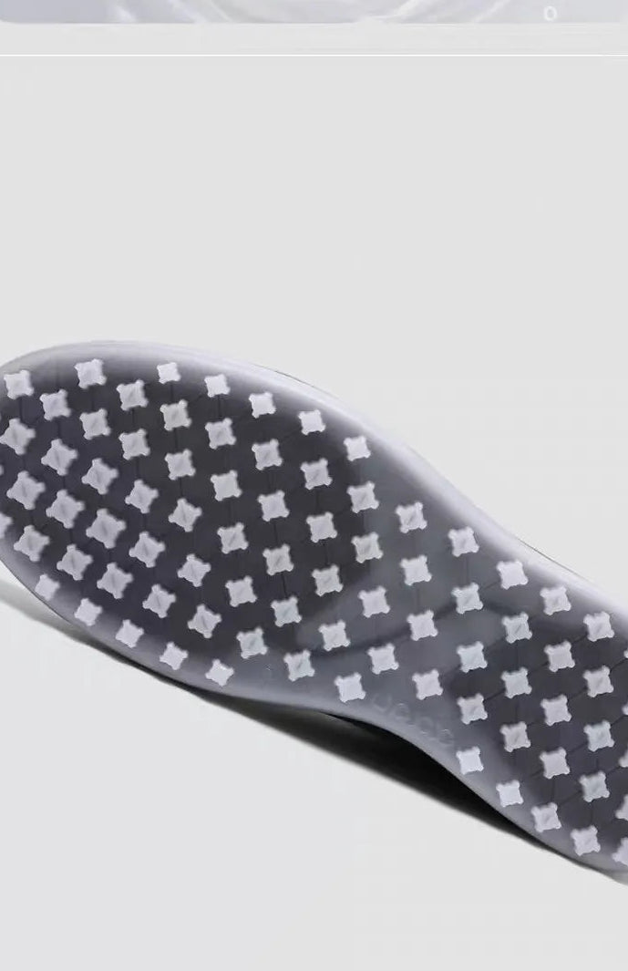 Close-up of the outsole of a sneaker, showing a pattern of small white square studs on a translucent gray and white rubber base, photographed against a light gray background.