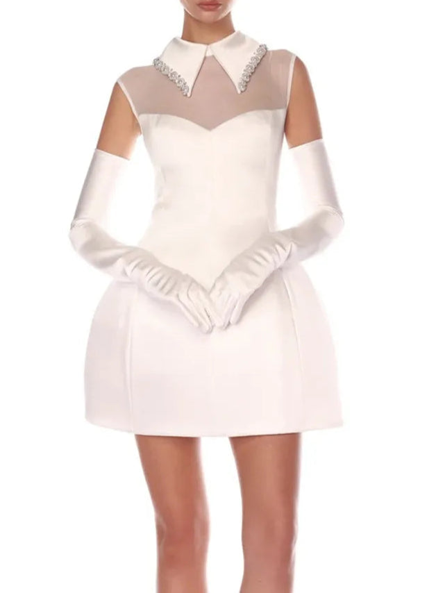 A woman wearing a white sleeveless mini dress with a square neckline, adorned with pearl and diamond beading, designed for evening or party wear.