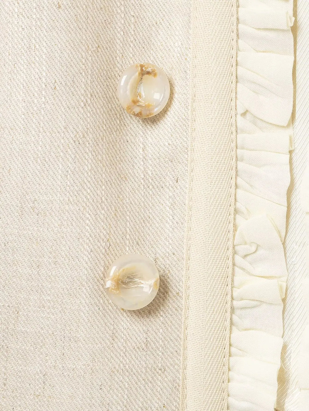 Beige blazer close-up with gold-tone buttons and inner ruffle trim