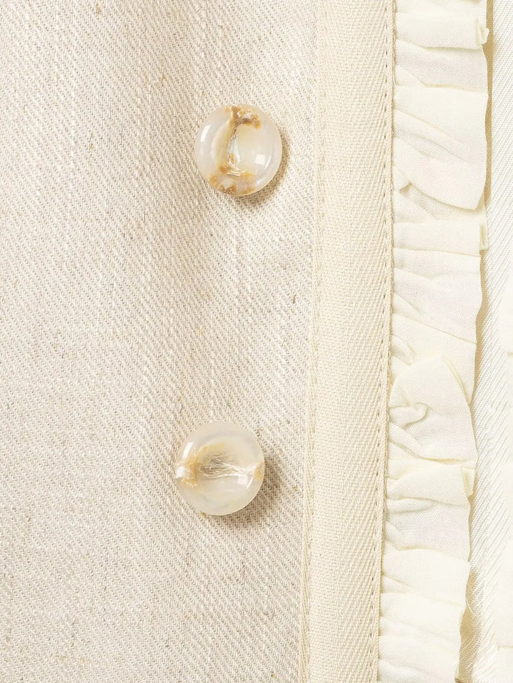 Beige blazer close-up with gold-tone buttons and inner ruffle trim
