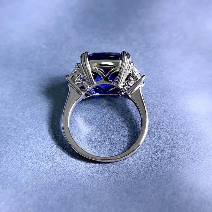 Sterling silver ring with openwork prongs around blue center stone and clear side gems