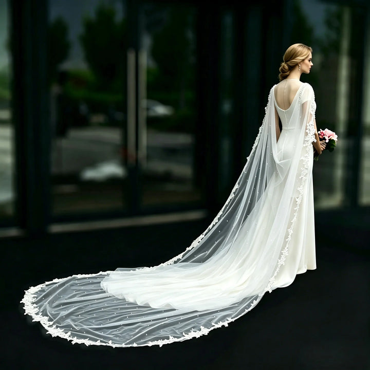 White sheer bridal cape draping over the back with lace-edged border and pearl-like beading