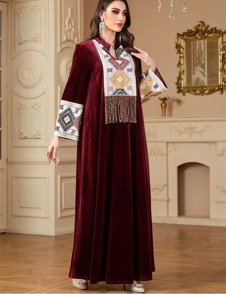 Woman wearing a burgundy abaya with intricate patterns in a decorated room.