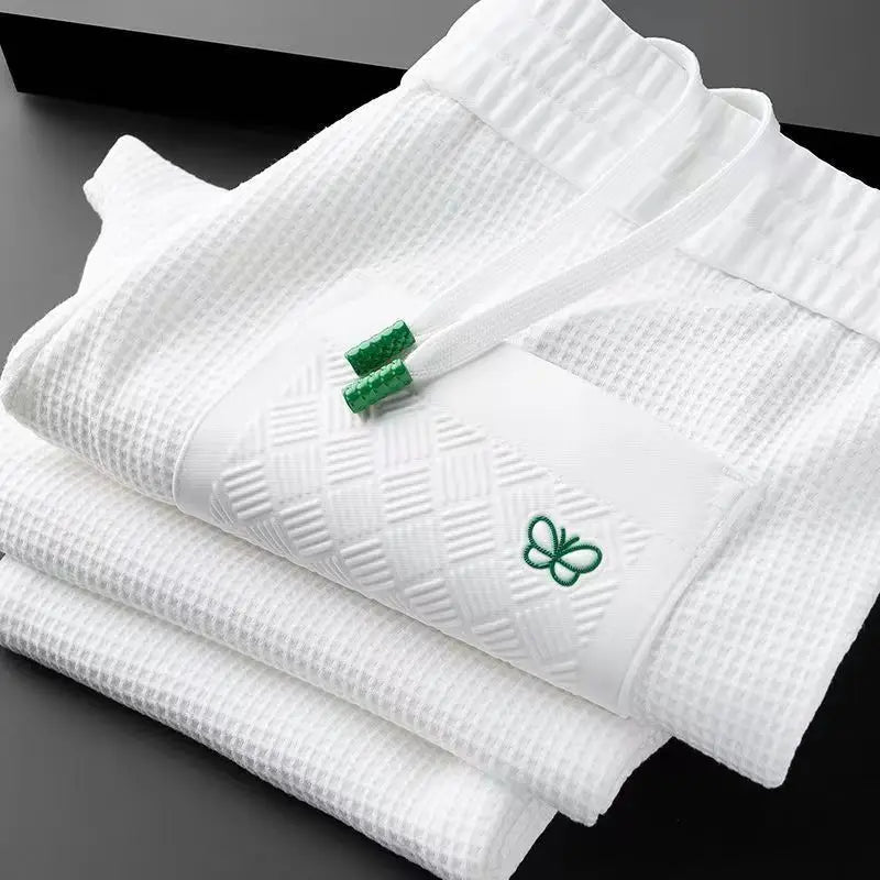 White cotton track pants folded with green butterfly logo on waffle-textured fabric
